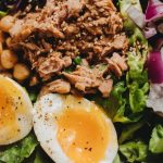 Close-up of a nutritious salad with tuna, soft-boiled eggs, and fresh vegetables.